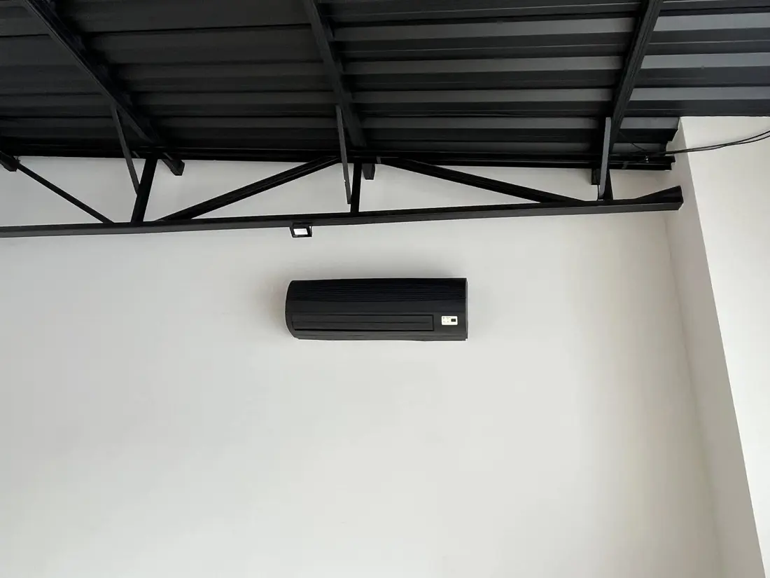 Ar-condicionado split de cor escura instalado em parede sob estrutura metálica de cobertura